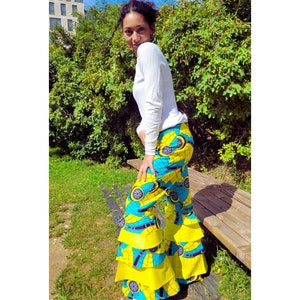 May include: A woman wearing a white long-sleeved shirt and yellow and blue patterned bell bottom pants with multiple tiers. The pants have a floral design.
