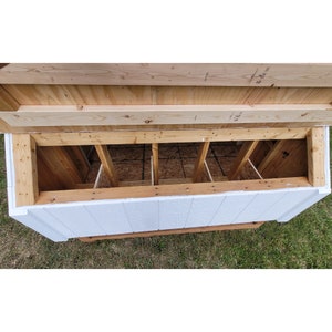May include: A white wooden chicken coop with a hinged top that opens to reveal four nesting boxes. The nesting boxes are made of wood and have a wire mesh floor.