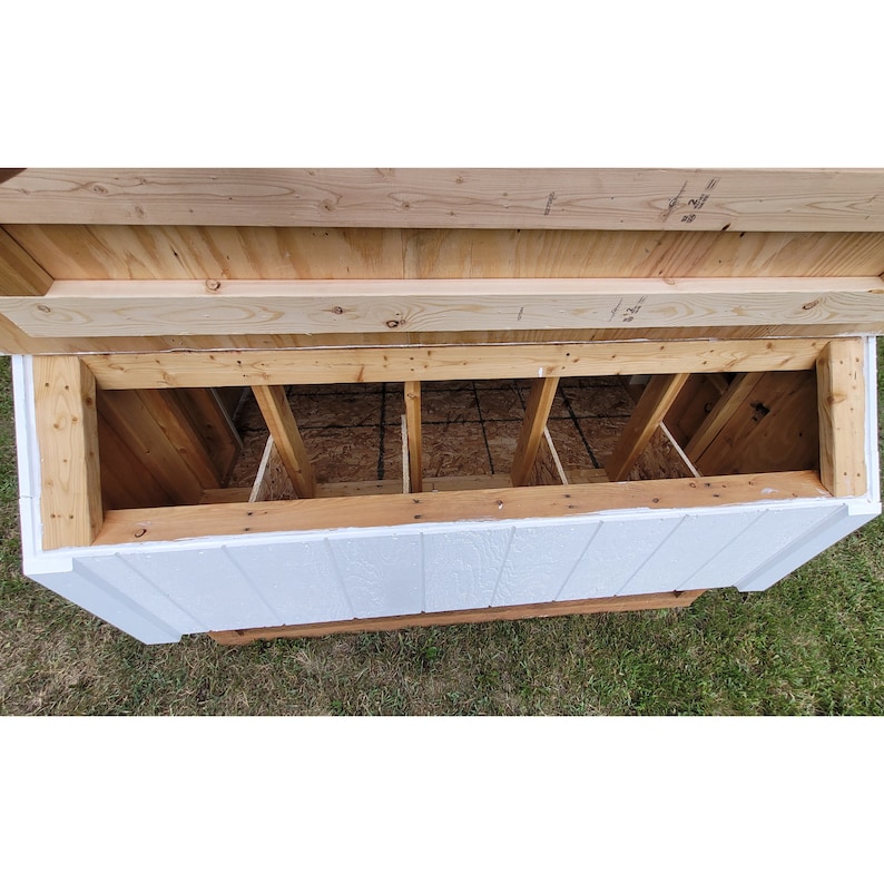 May include: A white wooden chicken coop with a hinged top that opens to reveal four nesting boxes. The nesting boxes are made of wood and have a wire mesh floor.