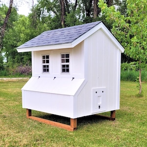 May include: White wooden chicken coop with a black shingled roof. The coop has two windows, a nesting box, and a door. The coop is sitting on a wooden base.