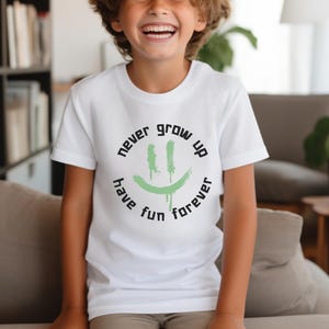 May include: White t-shirt with a green smiley face graphic and the text "never grow up have fun forever".