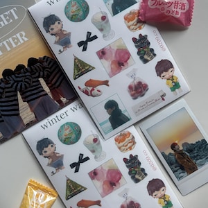 May include: A collection of stickers and a photograph featuring various illustrations, including a doll, a sundae, and a koi fish. The stickers have the text "winter waves" and Japanese text. A pink candy wrapper is also present.