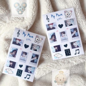 May include: Two white paper sheets with photos, text, and illustrations, including the words "My Muse" and a musical note. A small plush angel and a blue mouse sticker are also visible. The background is a white, fluffy blanket.