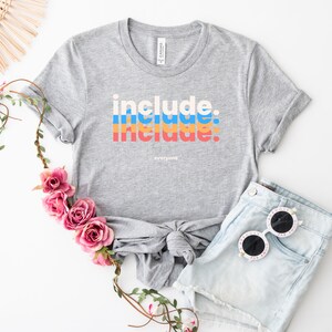 May include: A gray t-shirt with the text "include: include: everyone" in a retro rainbow design.
