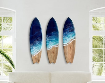 Op de afbeelding: Drie blauwe en witte resin surfboard wanddecoraties met een houtnerf afwerking. De surfboards zijn in een rij op een witte muur geplaatst.