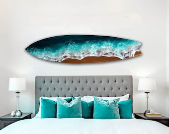 Op de afbeelding: Een wit bed met een grijs hoofdeinde en tealblauwe kussens. Een surfboard met een hars ocean wave design hangt boven het bed.