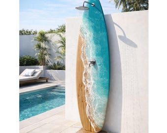 May include: An outdoor shower in the shape of a surfboard, featuring a turquoise and wood grain design. The shower head is positioned above the board, with water flowing down. The shower is set against a white wall, with a pool and palm trees visible.