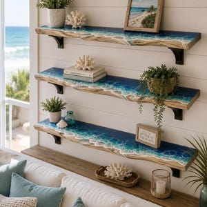 Puede incluir: Tres estantes de pared con bordes naturales que presentan un diseño de olas oceánicas en resina azul y blanca. Cada estante está sostenido por soportes de metal negro y contiene varios objetos decorativos como plantas y coral.
