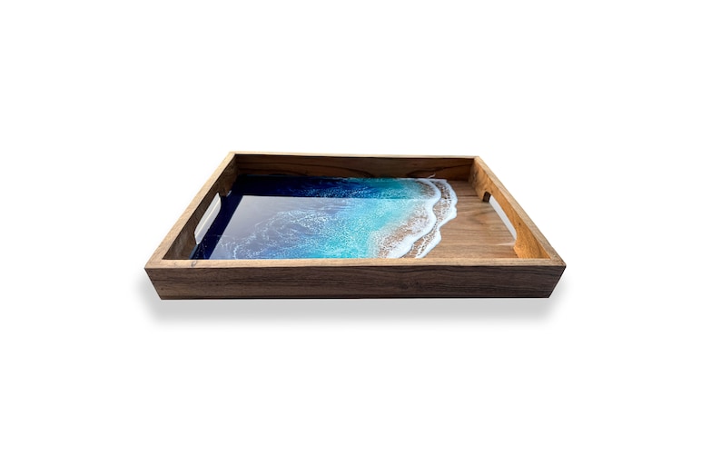 May include: Wooden serving tray with a resin ocean design. The tray features a dark brown wooden frame and handles. The interior has a blue and white resin design that resembles a beach scene.