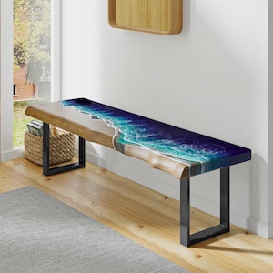 Op de afbeelding: Een houten bank met een blauw en wit epoxyhars blad dat lijkt op een oceaan golf. De bank heeft een zwart metalen frame en staat op een houten vloer.