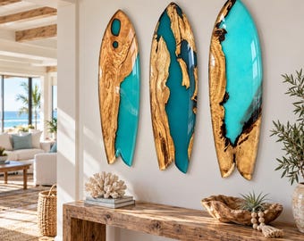Op de afbeelding: Drie aan de muur gemonteerde kunstwerken in de vorm van een surfplank, bestaande uit natuurlijk houtnerf gecombineerd met doorschijnende turquoise hars. Elk stuk toont een unieke organische houten rand met een gladde, glanzende afwerking.