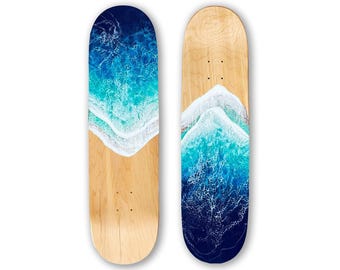 May include: Two skateboards with ocean-themed artwork. One features a dark blue to light blue gradient with white foam, the other has a similar design. The bottom half of each board is natural wood.