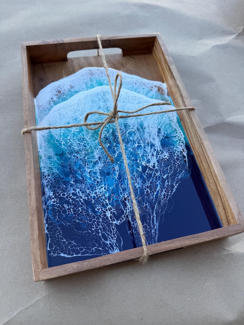 May include: A wooden serving tray with three coasters. The coasters have a blue and white ocean wave design. The tray and coasters are tied together with twine. The coasters have a glossy finish.