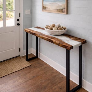 May include: A wooden console table with a live edge and a white resin river. The table has black metal legs and a bowl filled with decorative spheres. A framed beach scene hangs on the wall above the table.