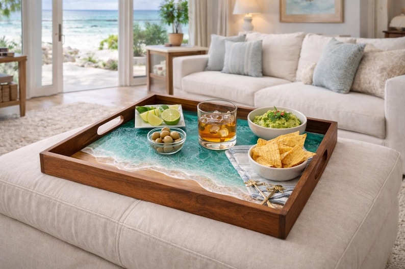 May include: A wooden serving tray with a beach-themed design, featuring a turquoise and white resin ocean scene. The tray holds a glass of whiskey, guacamole, chips, olives, and lime slices, perfect for entertaining.