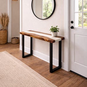 May include: A modern entryway with a wooden console table featuring a live edge design with a white resin inlay. The table has black metal legs. A round black mirror hangs above the table, and a small potted plant sits on top.
