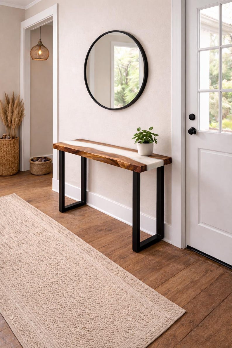 May include: A modern entryway with a wooden console table featuring a live edge design with a white resin inlay. The table has black metal legs. A round black mirror hangs above the table, and a small potted plant sits on top.