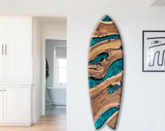 Op de afbeelding: Een decoratief houten surfboard met een uniek ontwerp. Het board combineert natuurlijke houtnerf met helder turquoise hars, wat een opvallend contrast creëert. Het surfboard is aan een witte muur bevestigd.