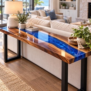 May include: A long rectangular console table featuring a natural wood slab top with a vibrant blue epoxy resin river running through the center. The table is supported by two sturdy black metal U-shaped legs and has a smooth, polished finish.