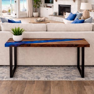 May include: A modern wooden console table with a dark walnut finish and a vibrant blue resin river. The table has black metal legs and a rectangular shape. A small potted plant sits on the table.