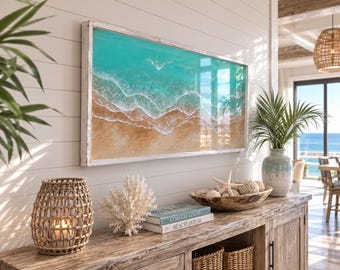 May include: A rectangular wall art piece featuring an aerial view of turquoise ocean waves crashing onto a sandy beach, enclosed in a white wooden frame. The artwork displays layered blue water, white sea foam, and textured tan sand.