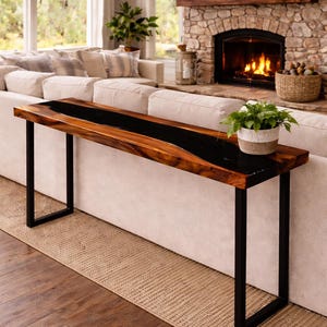 May include: A modern, wooden console table with a black epoxy resin inlay. The table has a rectangular top and black metal legs. A small potted plant sits on the table. The table is placed in front of a white sofa.