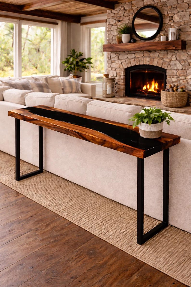 May include: A modern, wooden console table with a black epoxy resin inlay. The table has a rectangular top and black metal legs. A small potted plant sits on the table. The table is placed in front of a white sofa.