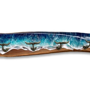 May include: A wooden wall hook with a blue and white resin ocean wave design. The hook has four whale tail shaped hooks.