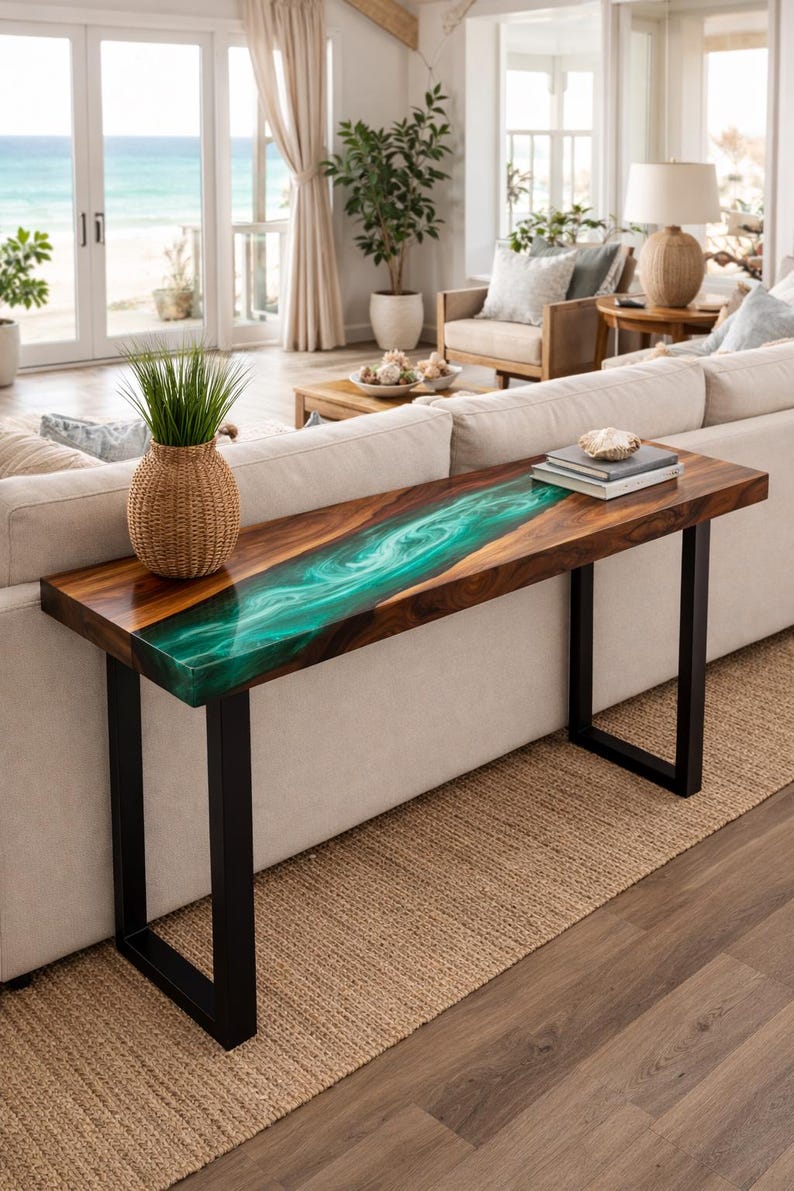 May include: A wooden console table with a vibrant teal epoxy resin river design. The table has a dark wood finish, black metal legs, and a woven basket with greenery. Books and a decorative shell sit on top.