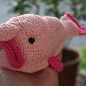 Puede incluir: Un juguete de pez rosa claro tejido a mano con detalles en rosa oscuro. El juguete presenta una lengua, aletas y un pequeño ojo de botón negro. El pez es suave y afelpado, ideal para la colección de juguetes de un niño.