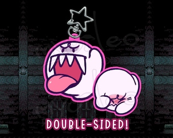 May include: Double-sided keychain featuring two cartoon ghosts with pink accents. One ghost has an open mouth with a pink tongue, and the other is blushing. The keychain has a star-shaped clasp and the text "DOUBLE-SIDED!"