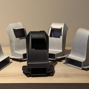 May include: An assortment of five plastic components, with a mix of gray and black colors. The objects have a geometric design with rectangular and curved shapes. They are arranged on a wooden surface.