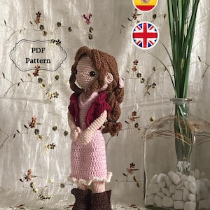 May include: Crochet doll pattern in PDF format. The doll is wearing a pink dress, a burgundy vest, and brown boots. The doll has brown hair and brown eyes. The pattern is available in both English and Spanish.