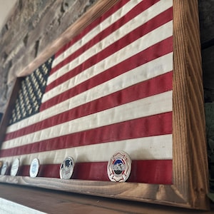 K&ouml;nnte beinhalten: Amerikanische Flagge in einem Holzrahmen. Die Flagge hat rote und wei&szlig;e Streifen und ein blaues Feld mit wei&szlig;en Sternen. Mehrere Gedenkm&uuml;nzen sind darunter ausgestellt und verleihen der patriotischen Dekoration eine pers&ouml;nliche Note.