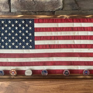 K&ouml;nnte beinhalten: Ein gerahmter amerikanischer Flagge mit einem Holzrahmen. Die Flagge hat rote und wei&szlig;e Streifen und ein blaues Feld mit wei&szlig;en Sternen. Darunter befinden sich sechs runde M&uuml;nzen mit verschiedenen Designs.