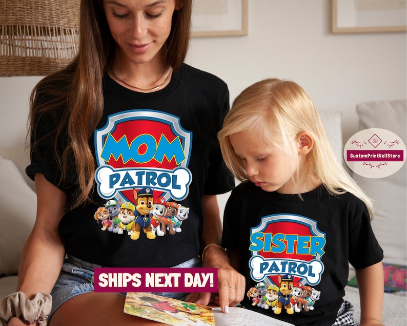 May include: Two black t-shirts with a Paw Patrol theme. The larger shirt says "Mom Patrol" with a Paw Patrol logo and the smaller shirt says "Sister Patrol" with a Paw Patrol logo.