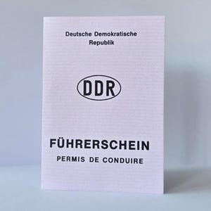 Puede incluir: Un documento de permiso de conducir de Alemania Oriental de color rosa claro con el texto Deutsche Demokratische Republik, un emblema ovalado central DDR y las palabras FÜHRERSCHEIN PERMIS DE CONDUIRE en letras negras en la portada.