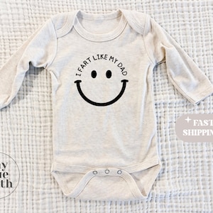 May include: A beige long-sleeve baby onesie with a black smiley face and the text "I fart like my dad".