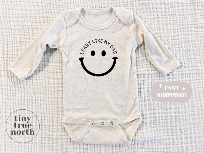 May include: A beige long-sleeve baby onesie with a black smiley face and the text "I fart like my dad".