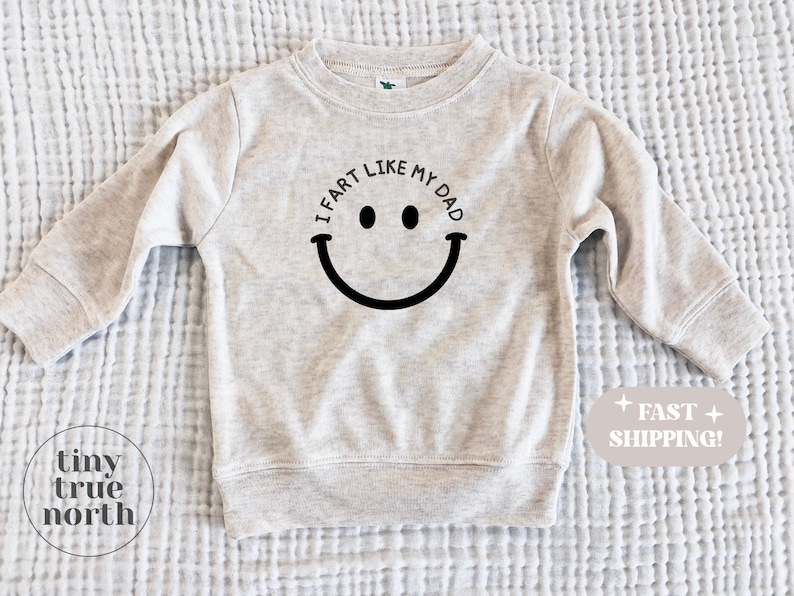May include: A light grey sweatshirt with the text "I fart like my dad" and a black smiley face graphic.
