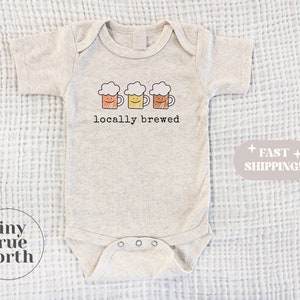 May include: A light grey baby onesie with a graphic of three cartoon beer mugs and the text "locally brewed".