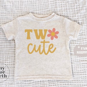 May include: A light grey short-sleeved t-shirt with the text "TWO cute" in yellow with a pink flower graphic.
