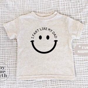 May include: A light gray t-shirt with a black smiley face and the text "I fart like my dad".
