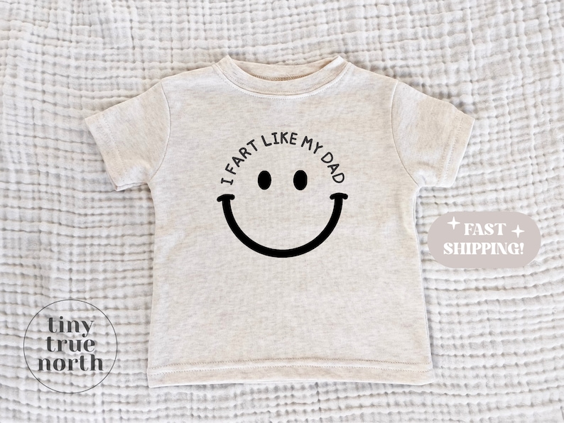 May include: A light gray t-shirt with a black smiley face and the text "I fart like my dad".