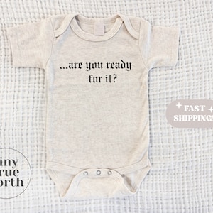 May include: A beige baby onesie with short sleeves and the text "...are you ready for it?" printed in black.