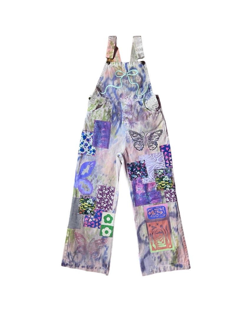 Op de afbeelding: Paarse en groene tie-dye denim overalls met vlinder- en bloemenpatches.