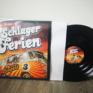 Puede incluir: Un disco de vinilo negro con una portada de álbum colorida que presenta una camioneta Volkswagen vintage con el texto "Schlager Ferien" y "Beatles Pimpels 3".