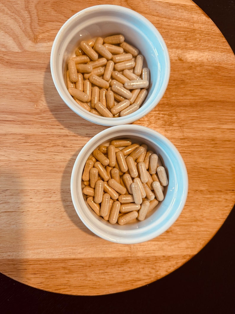 Peut inclure: Deux bols blancs remplis de capsules beiges. Les bols sont sur une surface en bois.
