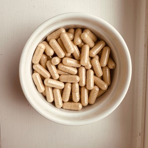 Peut inclure: Un bol en c&eacute;ramique blanche rempli d'une grande quantit&eacute; de capsules beiges.
