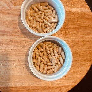 Peut inclure: Deux bols en c&eacute;ramique blanche remplis de capsules beiges. Les bols sont sur une surface en bois.